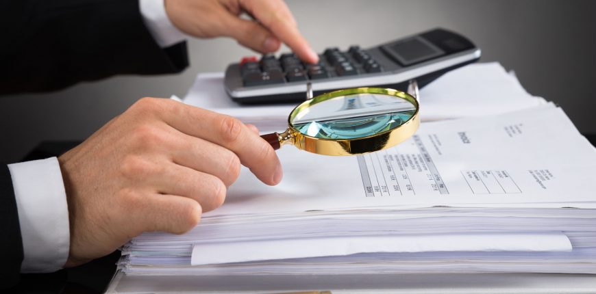 45058557 - close-up of businessperson hands checking invoice with magnifying glass at desk
