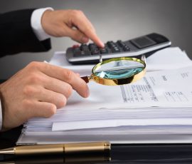 45058557 - close-up of businessperson hands checking invoice with magnifying glass at desk